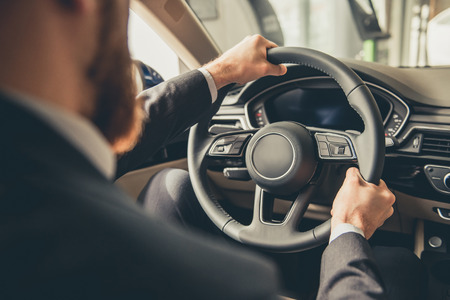 Cropped image of handsome bearded businessman sitting in a new car in car dealershipの写真素材