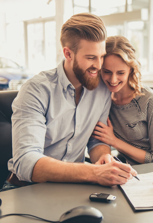 Visiting car dealership. Beautiful couple is talking to sales manager, signing document and smilingの写真素材