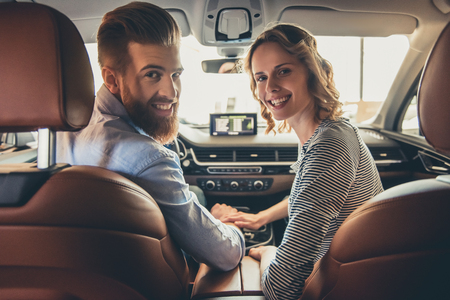 Visiting car dealership. Beautiful couple is looking at camera and smiling while sitting in their new carの写真素材