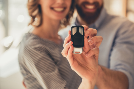 Visiting car dealership. Beautiful couple is holding a key of their new car, looking at camera and smilingの写真素材