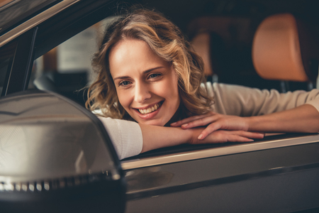 Beautiful young woman looking at the car side mirror and smiling while sitting in the new car in dealershipの写真素材