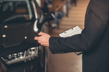 Cropped image of businessman holding a car key while standing in car dealershipの写真素材
