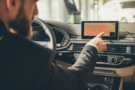 Handsome bearded businessman is using a digital map while driving the car
