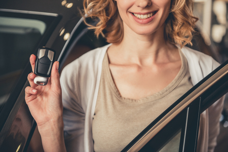 Cropped image of beautiful young woman holding a key and smiling while standing near the new car in car dealershipの写真素材