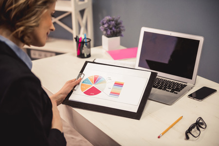 Beautiful pregnant business woman in suit is studying documents and touching her tummy while working in officeの写真素材