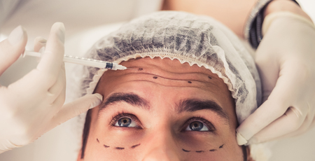 Handsome man is getting face skin treatment. Doctor in medical gloves is making an injection, close-upの写真素材