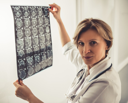 Beautiful mature doctor in white coat is holding x ray image and looking at cameraの写真素材