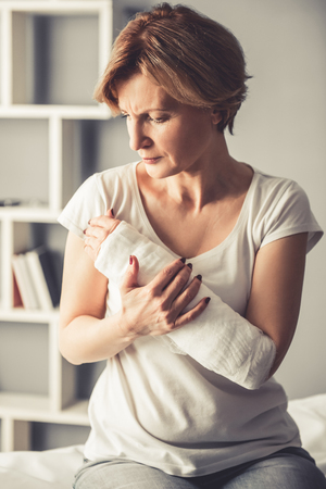 Beautiful mature woman with her arm in gypsum is sitting at the traumatologistの写真素材