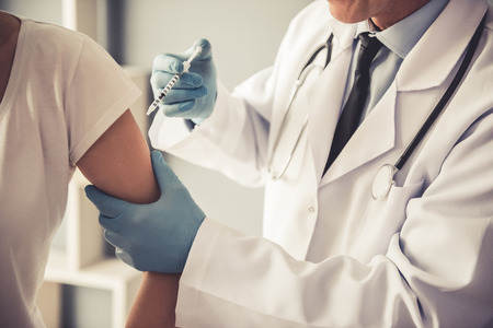 Cropped image of handsome mature doctor in protective gloves making woman an injectionの写真素材
