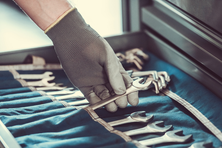 Cropped image of mechanic in working gloves choosing tool while repairing car in auto serviceの写真素材