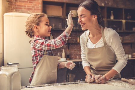 Beautiful young mom and her cute little daughter are playing and smiling while baking in kitchen at homeの写真素材