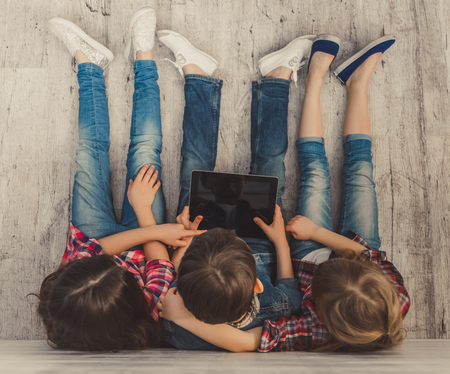 Top view of cheerful kids using a digital tablet while sitting on the wooden floorの写真素材