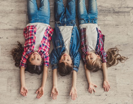 Top view of cheerful kids looking at camera and smiling while lying on the wooden floorの写真素材