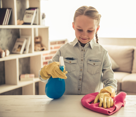 Pretty little girl in protective gloves is using a sprayer and a rag while cleaning her houseの写真素材