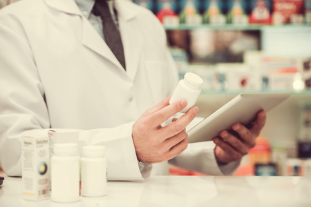 Cropped image of handsome pharmacist holding drugs and using a digital tablet while working in pharmacyの写真素材