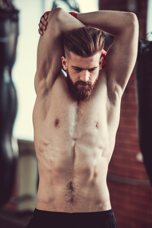 Handsome bearded boxer with bare torso is stretching before working out at the fight clubの写真素材