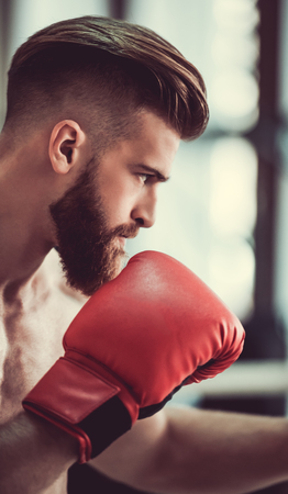 Side view of handsome bearded boxer with bare torso in red boxing gloves ready to fightの写真素材