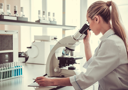 Beautiful female medical doctor is using a microscope while working at the lab