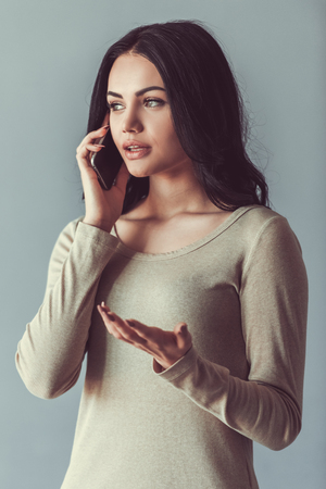Beautiful young woman is talking on the mobile phone, on gray backgroundの写真素材