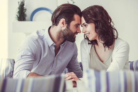 Beautiful young woman and man in love are touching with their foreheads, looking at each other and smiling while resting in cafeの写真素材