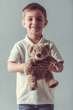 Cute little boy is holding a teddy bear, looking at camera and smiling, on gray backgroundの写真素材