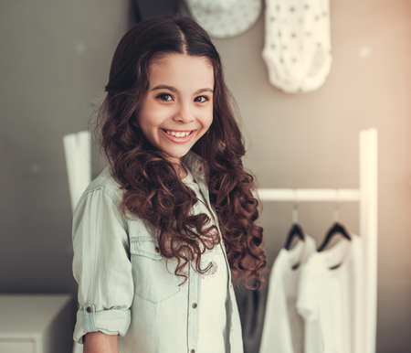 Beautiful school girl is looking at camera and smiling while standing in her roomの写真素材