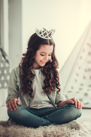 Beautiful school girl is smiling while sitting with a crown on her head in her roomの写真素材