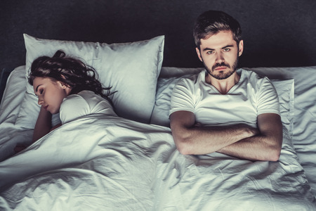 Young unhappy man and his girlfriend sleeping in bed.の写真素材
