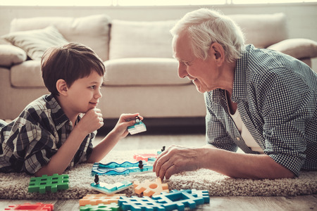 Grandpa and grandson are playing with toys, looking at each other and smiling while resting together at home