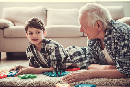 Grandpa and grandson are playing with toys while resting together at home. Boy is looking at camera and smilingの写真素材