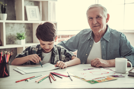 Handsome grandpa and grandson are drawing while spending time together at home. Old man is looking at camera and smilingの写真素材