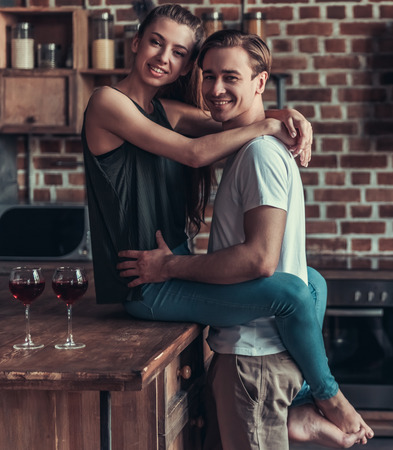 A young lovers couple drink wine during the celebration and embrace themselves at home in the kitchenの写真素材
