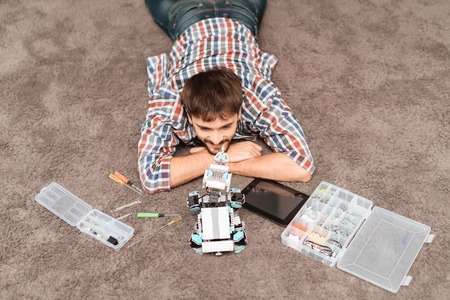 The guy is sitting on the floor. Next to it is a robot rhino, parts of robots and tools.の写真素材