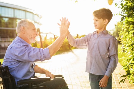 High five. The old man in a wheelchair greets his grandsonの写真素材