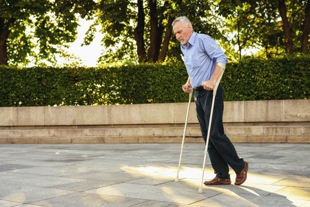 The old man on crutches strolls through the park. He is focusedの写真素材