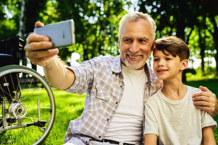 Happy old man doing selfie with his grandson sitting in park at picnicの写真素材