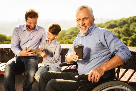 An old man in a wheelchair posing against his son and grandsonの写真素材