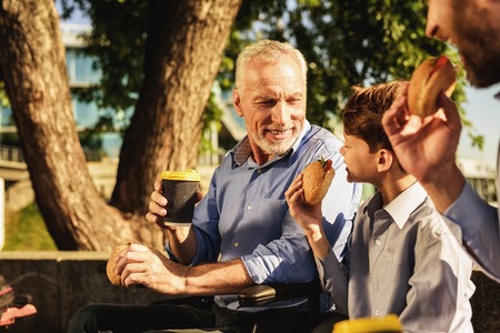 The old man in a wheelchair, his son and his grandson eat in the park