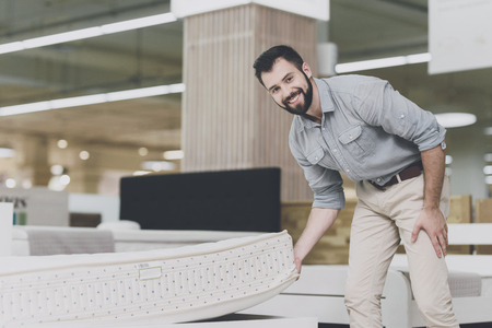 A man inspects a mattress in a mattress store. He lifted one of themの写真素材