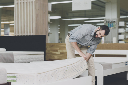 A man inspects a mattress in a mattress store. He lifted one of them