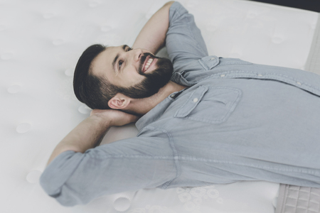 A man chooses a mattress for himself in the store. He is lying on one of themの写真素材