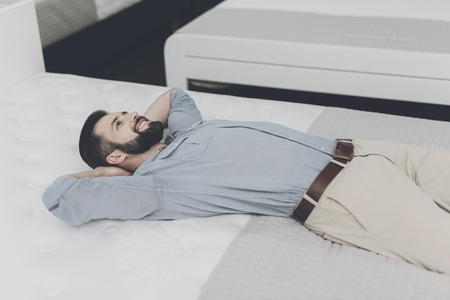 A man chooses a mattress for himself in the store. He is lying on one of themの写真素材