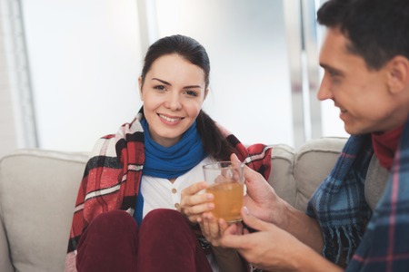 The couple is sitting on the couch wrapped in blankets. Man and woman are sick. A man gives a woman...