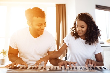 A black man sits in the living room of his apartment and plays a synthesizer. A girl is sitting next...