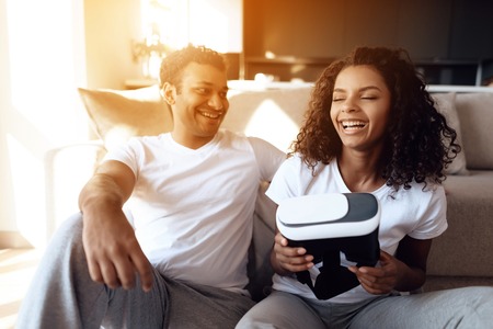 Black man and woman are sitting on the couch. A man and a woman hold a helmet of vr in their hands and dispose of it.の写真素材