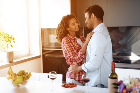 Black men and women in the kitchen at home cuddle. They look at each other with tenderness and love.の写真素材