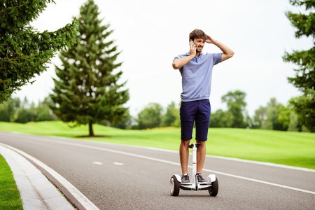 A man is driving through the park on a gyroboard. He is talking on the phoneの写真素材