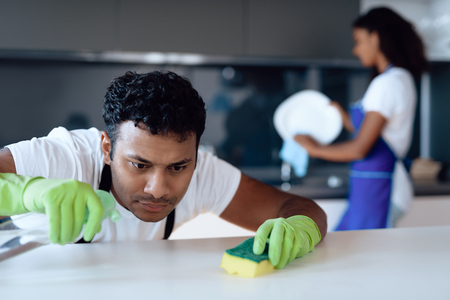 Black man and woman in the kitchen at home. They clean in the kitchen. A man washes the countertop with detergent.の写真素材
