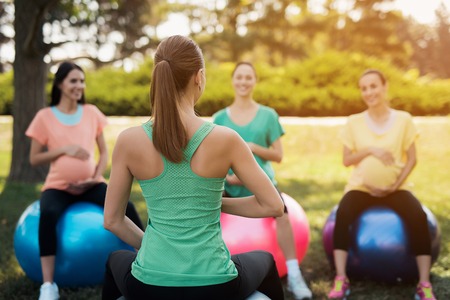 Pregnancy yoga. Three pregnant women in yoga in the park. They do the exercises with the coachの写真素材