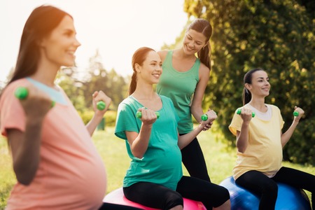 Pregnancy yoga. Three pregnant women are engaged in fitness in the park. They sit on balls for yogaの写真素材